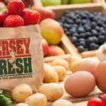 Basket overflowing with fresh produce: berries, apples, blueberries, and root vegetables.
