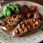 Grilled chicken breasts and roasted vegetables on a white plate with herbs.