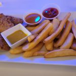 Fried chicken, french fries, and dipping sauces served on a white rectangular plate.