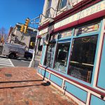 Street view of a restaurant facade with large windows and brick sidewalk under a clear blue sky.