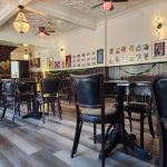 Interior of a restaurant with wooden floors, dark seating, and gallery wall art.