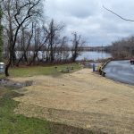 Park area overlooking a calm lake under an overcast sky with trees in the background.