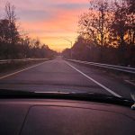 Sunset over a highway with vibrant orange and pink skies, viewed from inside a car.
