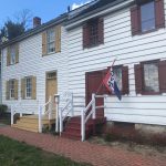 White historic building with red trim, steps leading to the entrance, and a flag displayed.