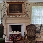 Elegant living room with floral wallpaper, fireplace, and antique furniture.