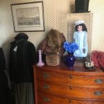 Vintage dresser with framed art, antique clothing, a doll, and decorative items.