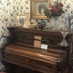 Antique wooden upright piano with decorative items and floral arrangement on top.