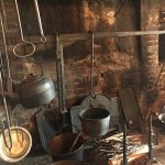 Rustic, dark kitchen interior with hanging pots and old metal tools against a brick wall.