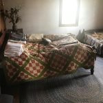 Cozy bedroom with a patterned quilt, natural light from a window.