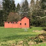 Red barn and outbuildings in a grassy field surrounded by trees.