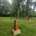 Stack of red bricks on a wooden crate in a grassy park setting with trees.