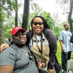 Two people, a man and a woman, stand outdoors in a park setting.