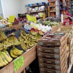 Produce display with bananas, avocados, and other fruits in a grocery store aisle.