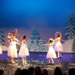 Dancers perform on a stage set with blue forest scenery.