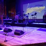Concert stage setup with band equipment and a large Ukrainian flag backdrop.