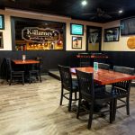 Bar interior with dark wood paneling, tables, and Killarney's pub signage.