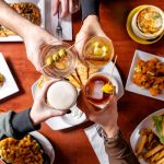People toasting with drinks around a table featuring pizza, appetizers, and snacks.