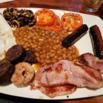Full English breakfast plate with eggs, sausage, beans, bacon, and tomatoes.