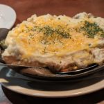 Cheesy baked casserole served hot in a black cast iron skillet on a white plate.