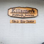 Wooden sign for Killarney's Public House on a white brick wall.