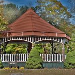 Red-roofed gazebo with white railings set among lush autumn trees.