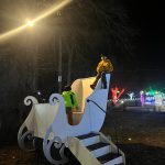 Children play on a white slide structure outdoors at night under bright lights.