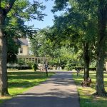Paved park path lined with trees leading toward a historic building in the distance.