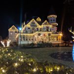Illuminated Victorian house with Christmas lights and a glowing reindeer sculpture at night.
