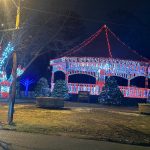 Christmas lights illuminate a gazebo and decorated trees at night.