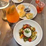 Orange juice, bread, and a plate of caprese-style salad with burrata cheese on a wooden table.