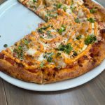Pepperoni and chicken pizza with melted cheese, herbs, and orange sauce on a white plate.