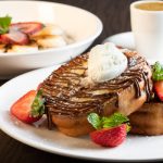Sweet French toast topped with whipped cream and chocolate drizzle, served with strawberries.