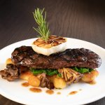 Grilled steak topped with caramelized onions, served with roasted potatoes and herbs.