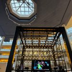 Modern atrium with large skylight overlooking a multi-level retail space featuring elaborate lighting.