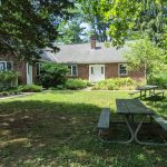 Single-story brick house with lawn and picnic tables under trees.