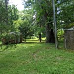 Small red cabin and brick building in a lush, green wooded yard.