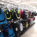 Assortment of backpacks displayed on metal shelving in a retail store aisle.