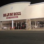 MJM Designer Shoes storefront at night with illuminated signage and large windows.