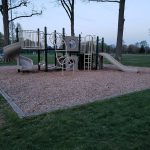 Playground structure with slides and climbing equipment set on a gravel base.