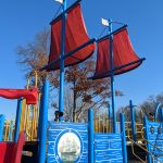 Colorful pirate ship playground structure with red sails under a clear blue sky.