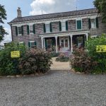 Historic gray wooden house with white trim and green shutters, fronted by a gravel driveway.