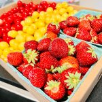 Mixed fresh berries in a cardboard box: red currants, yellow grapes, and strawberries.