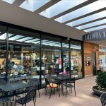 Modern bakery storefront with large windows, outdoor seating area, and "Lillipies Bakery" sign.