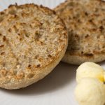 Two toasted bread rounds and small balls of butter on a white plate.