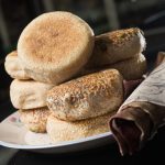 Stack of golden, sesame-crusted buns on a white plate with folded cloth napkin.
