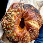 Seeded braided bread ring with pumpkin and sunflower seeds in a paper bag.