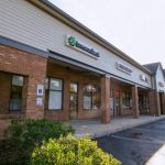 Commercial strip mall building with brick facade and storefronts under a bright sky.