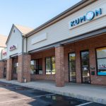 Kumon learning center exterior with multiple storefronts under a clear blue sky.