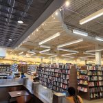 Interior view of a large bookstore with tall shelves, modern lighting, and customers browsing.