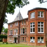 Victorian brick house with white trim and garden setting under green trees.